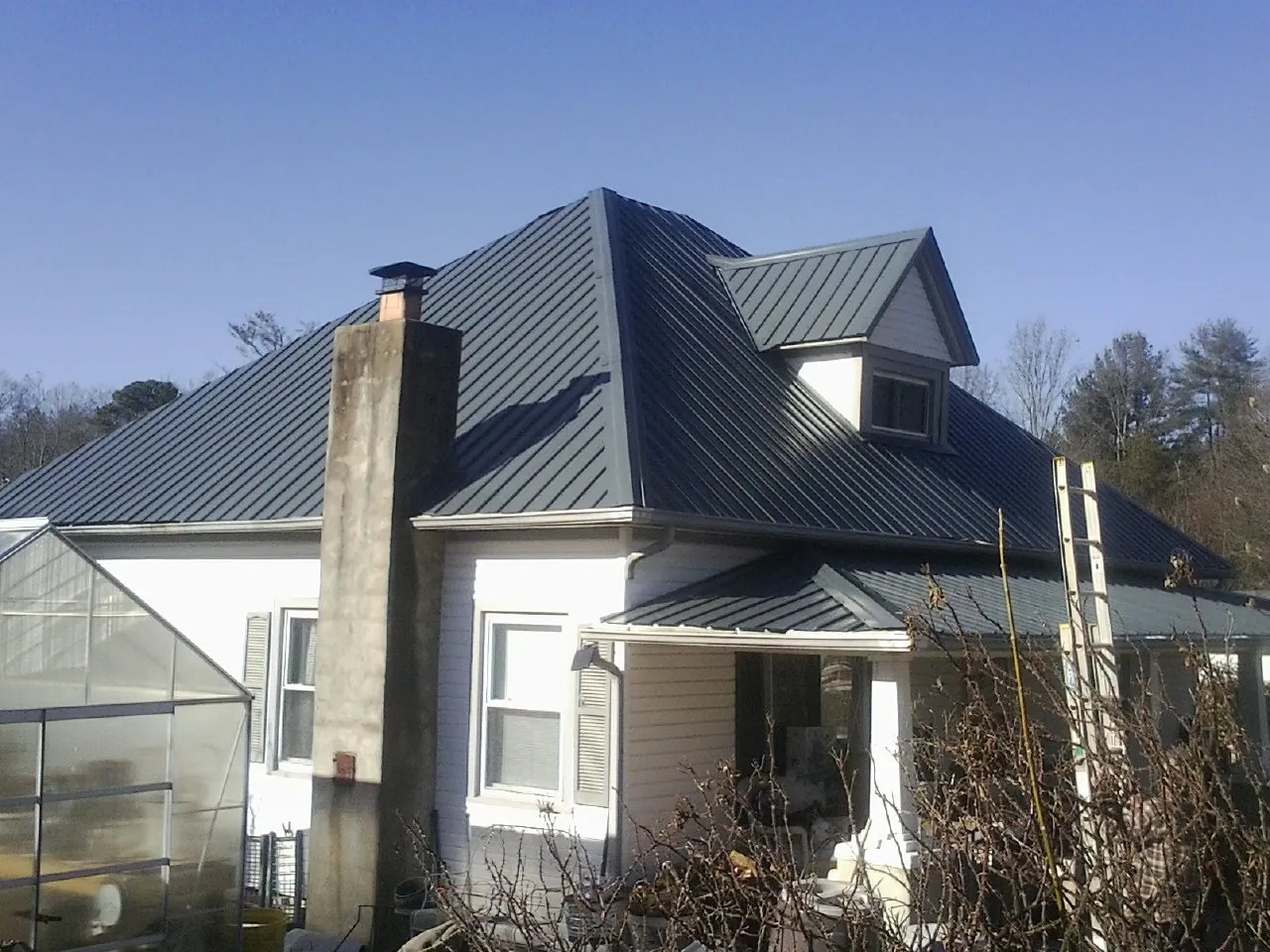 Dark blue standing seam metal roof on a white farmhouse with dormer — Slate & Tile Roof Repair by Roofing Brothers in Douglassville