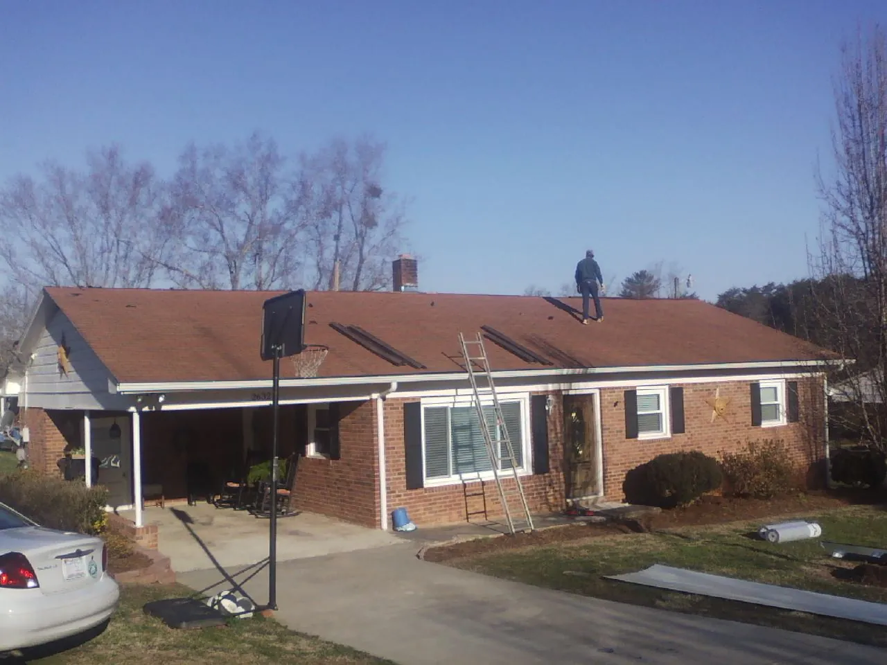 Roofer stripping a shingle roof on a brick ranch before metal panels in Douglassville