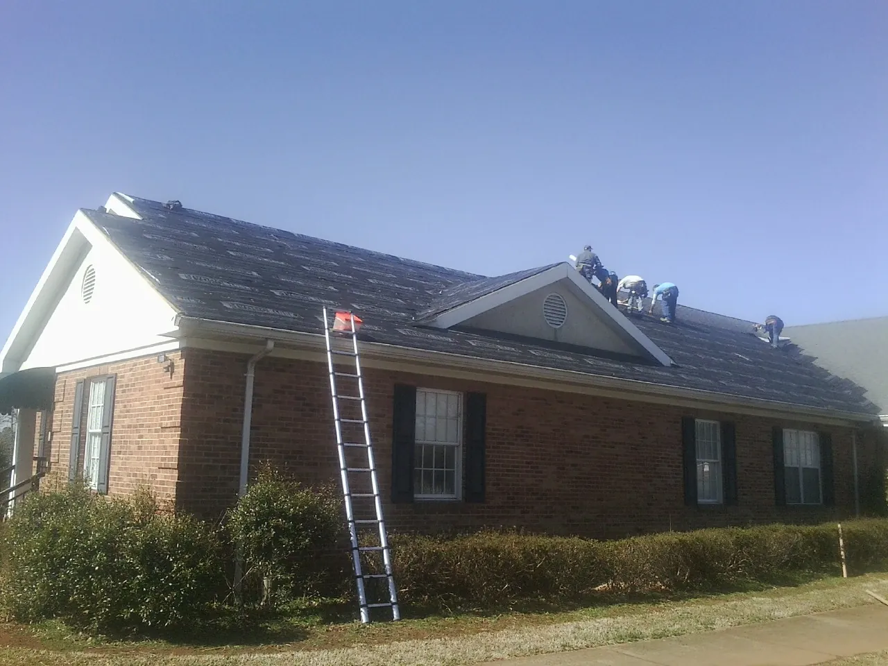 Crew tearing shingles off a brick ranch roof with a ladder set — Metal Roof Repair work by our crew in Douglassville