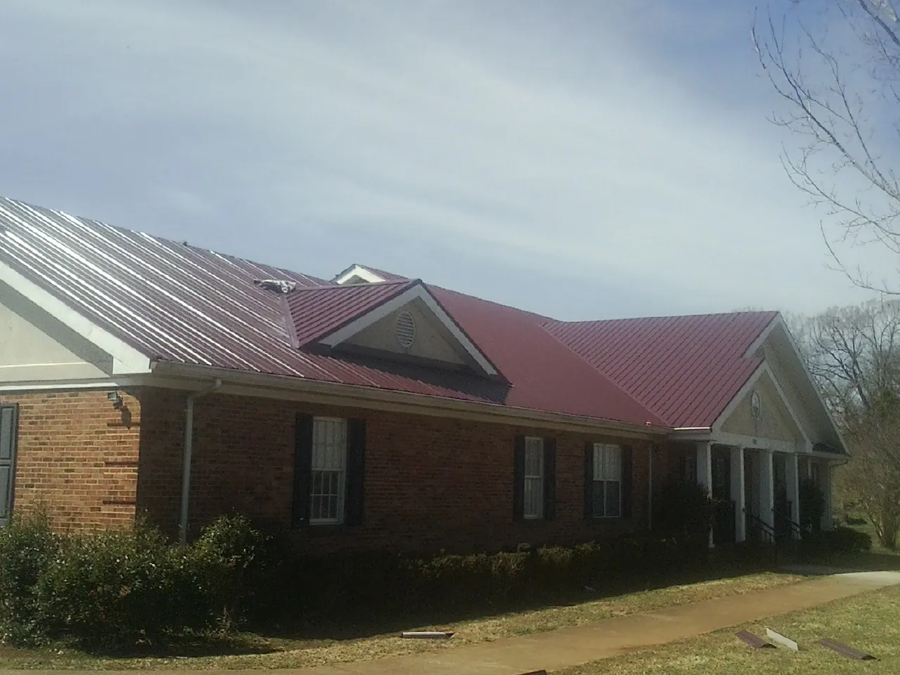 Red metal roof with gabled entries on a long brick building, from a Hail Damage Roof Repair job in Douglassville