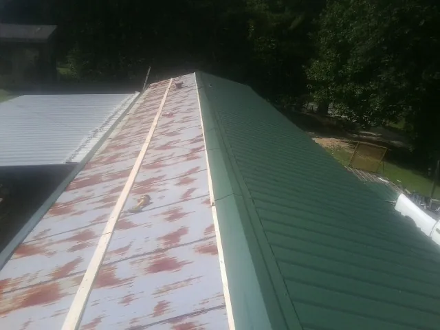 Old rusted panels beside newly installed green metal roofing — Wind Damage Roof Repair by Roofing Brothers in Douglassville