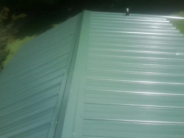 New green metal panels meeting at the ridge of a roof — Flat Roof Repair work by our crew in Douglassville