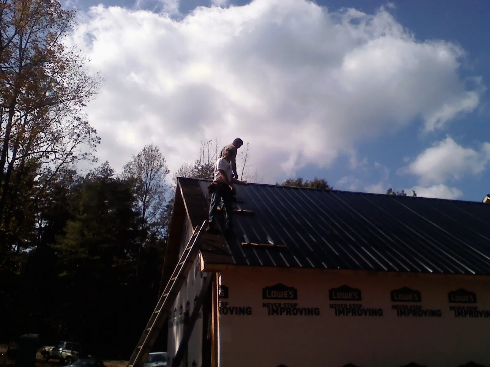 Roofer fastening dark metal panels high against a cloudy sky, from a Roof Inspection job in Douglassville
