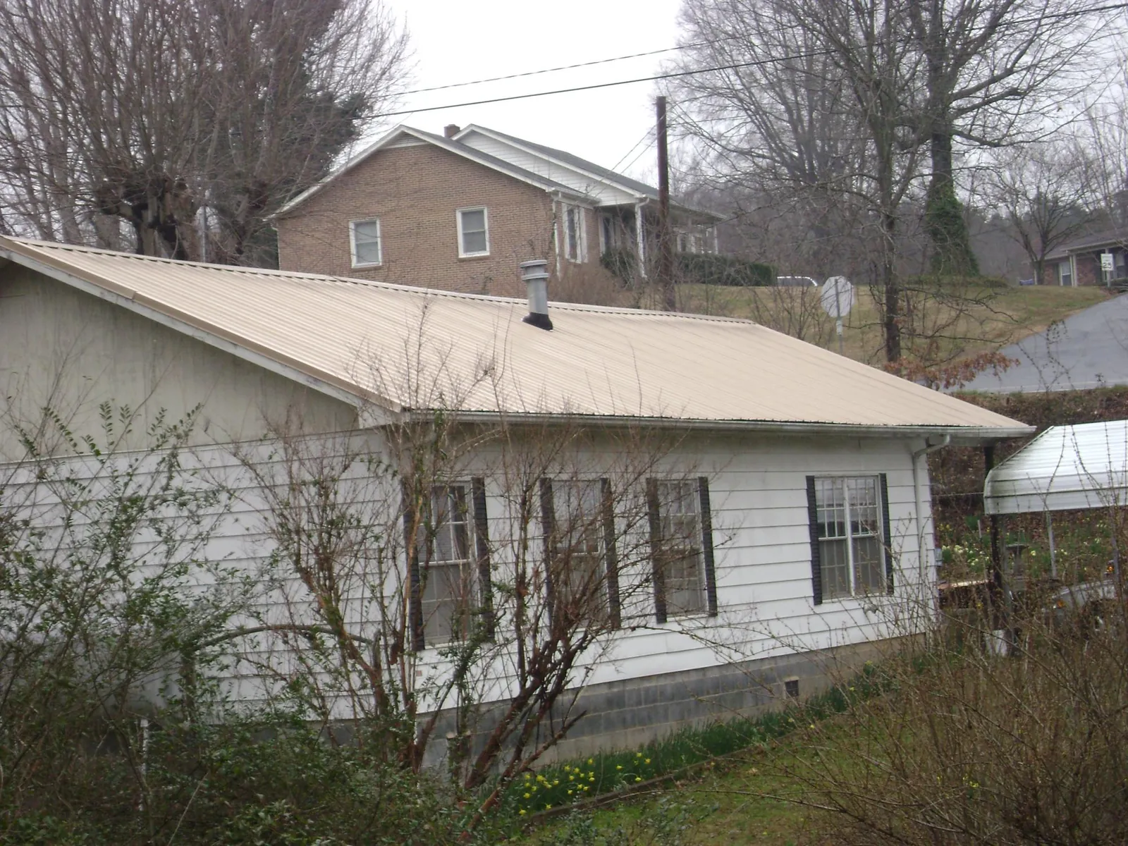 Tan metal roof on a white sided house set into a hillside — Commercial Roofing by Roofing Brothers in Douglassville