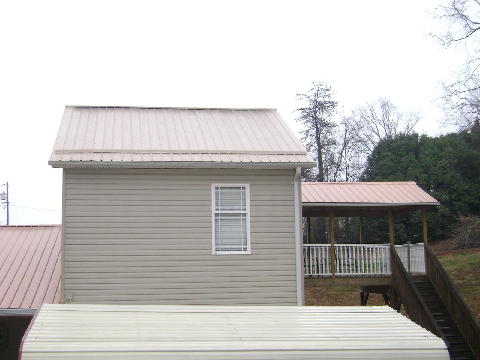 Tan metal roofs on a two story addition and attached porch, from a Roof Replacement job in Douglassville